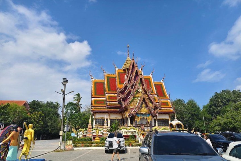 Ein traditioneller thailändischer Tempel mit aufwendiger Architektur, einer Statue einer Gottheit und einem gepflegten Garten. 4