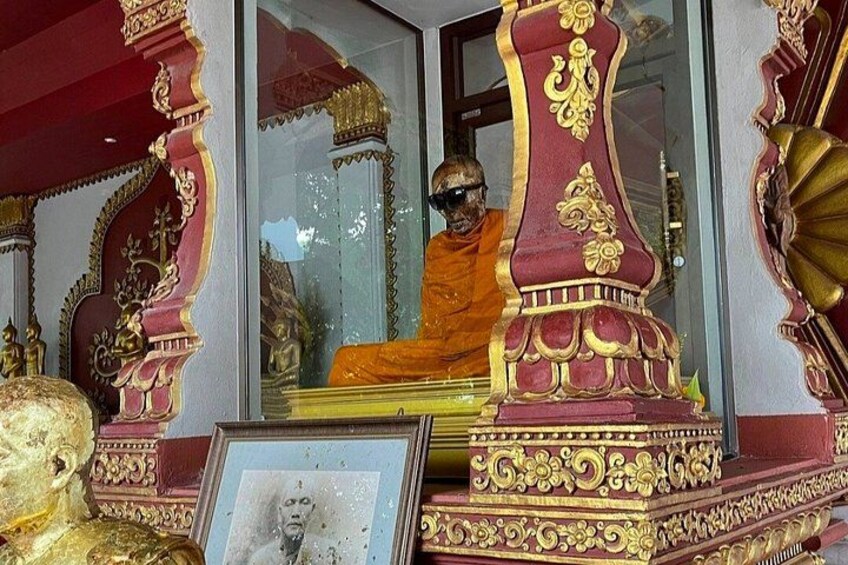 Ein reich verzierter Schrein mit aufwendigen goldenen und roten Säulen, einer sitzenden Figur in traditioneller Kleidung und einem gerahmten Porträt. 2