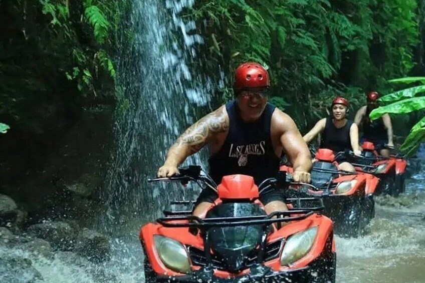 People riding ATVs through a water stream surrounded by greenery. 2