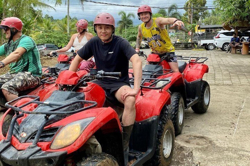 A group of people on red all-terrain vehicles (ATVs) in a rural setting with vegetation and a clear sky. 4