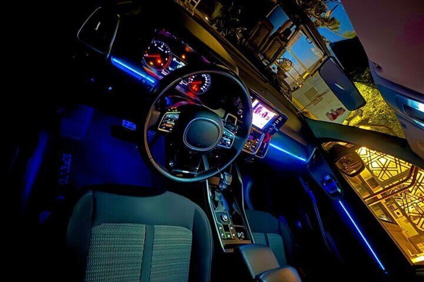 A car interior with a steering wheel, dashboard, and illuminated blue ambient lighting. 3