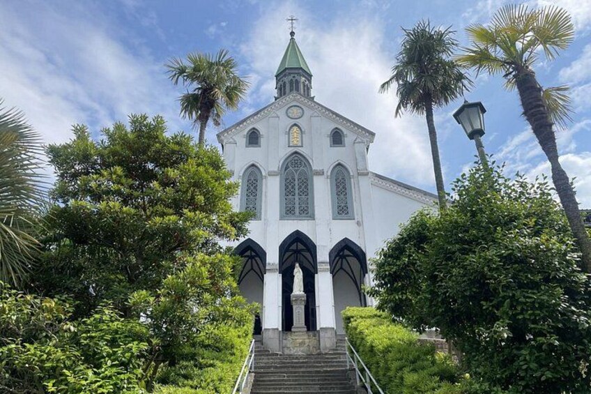 A white church with a green spire, surrounded by lush greenery and palm trees. 5