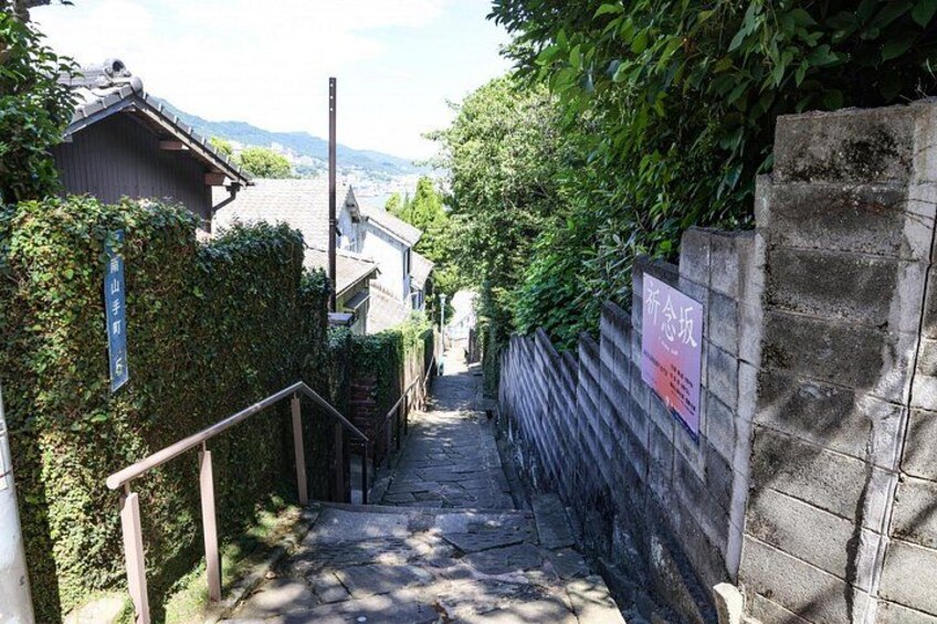 A narrow stairway leading uphill, flanked by a wooden fence and a stone wall with a sign. 2