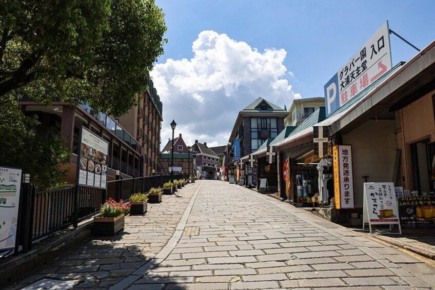 A cobblestone street lined with shops and a large tree on the left. 3