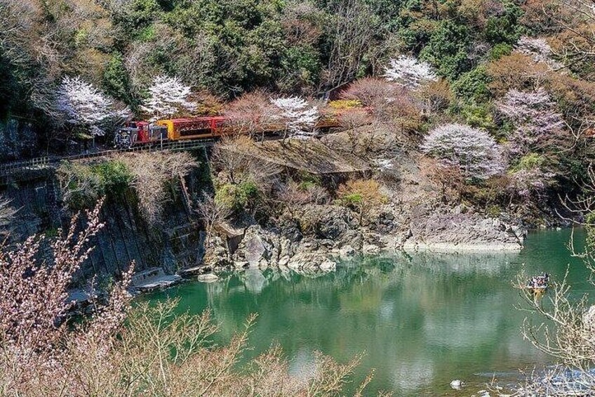 A train on a bridge over a calm body of water, surrounded by trees and rocky terrain. 5