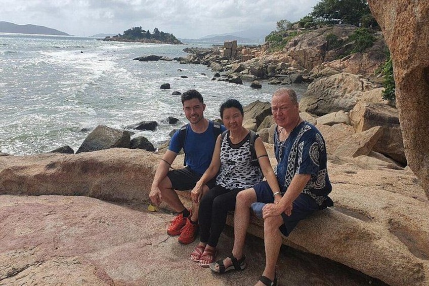 Three people sitting on a rock by the sea with waves crashing nearby. 3