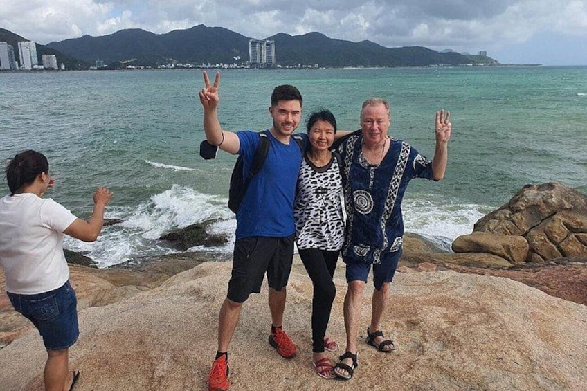 A group of people standing on a rocky shore with the ocean and mountains in the background. 4