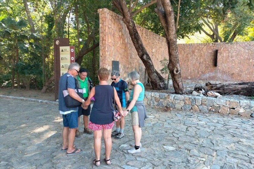 A group of people standing on a stone path in a wooded area with a stone wall and trees in the background. 3