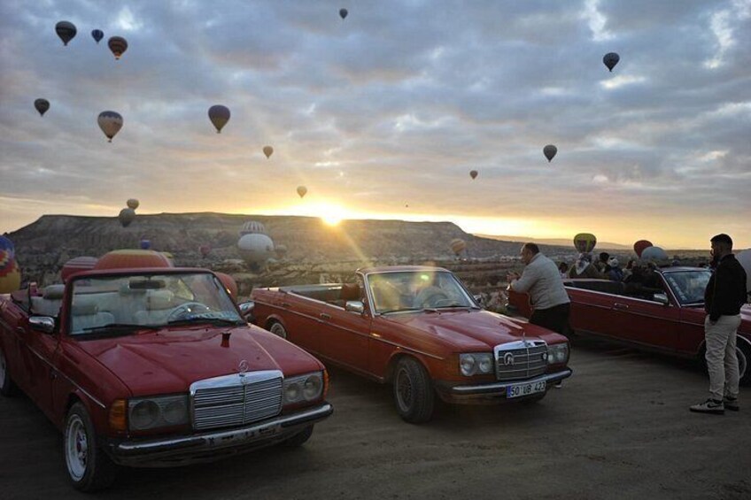 Vintage cars parked outdoors with hot air balloons in the background. 4