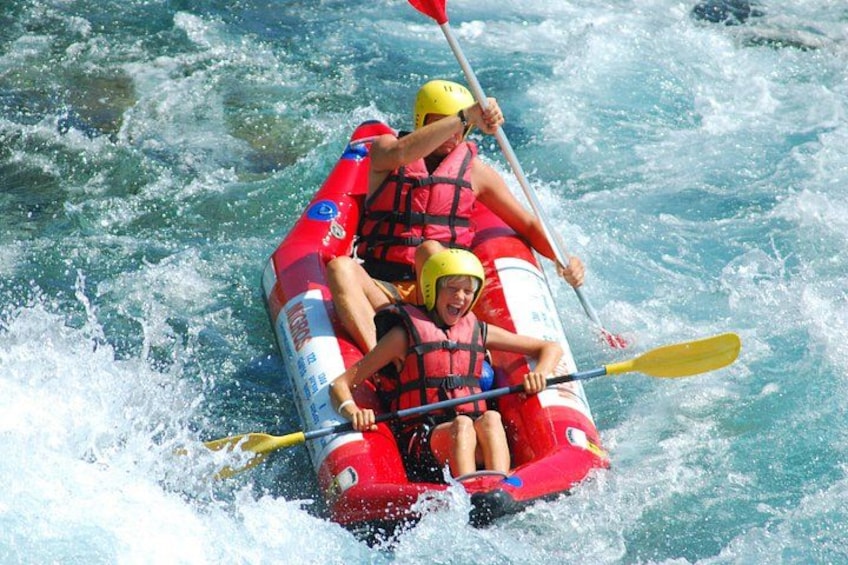 Two people in a red inflatable raft paddling on a river. 5