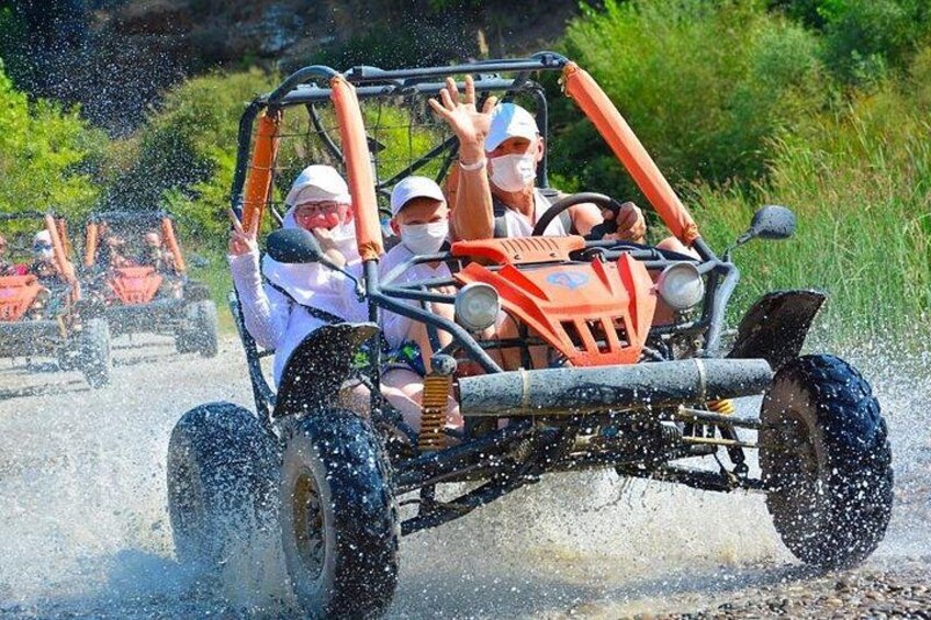 A group of people in a four-wheeled vehicle driving through water, splashing as they go. 3