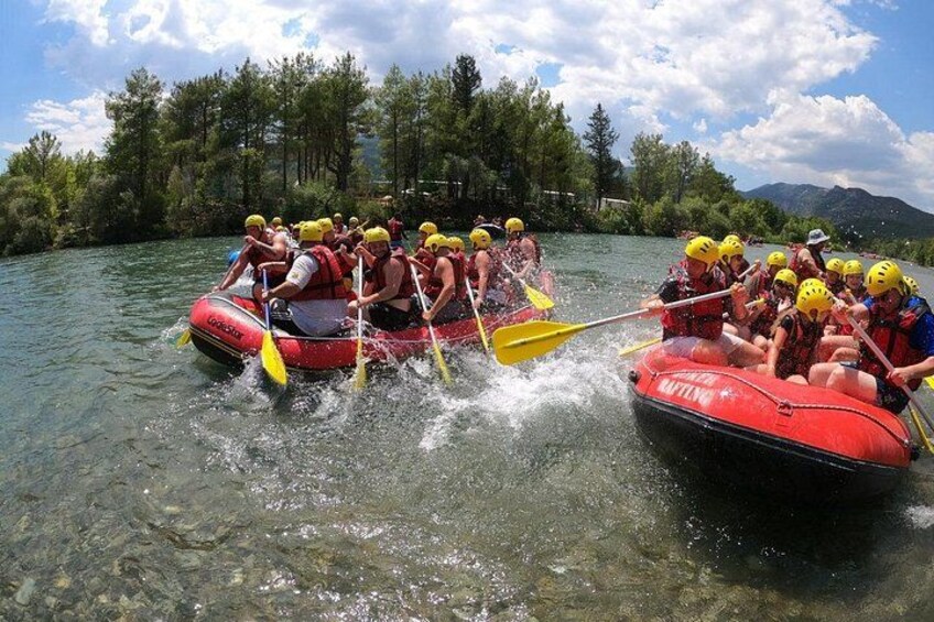 Two red inflatable rafts with people wearing helmets and life jackets, paddling on a river surrounded by trees. 4
