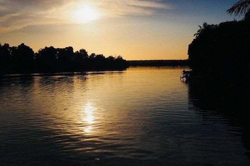 A calm lake at sunset with a silhouette of trees and a boat on the right. 4