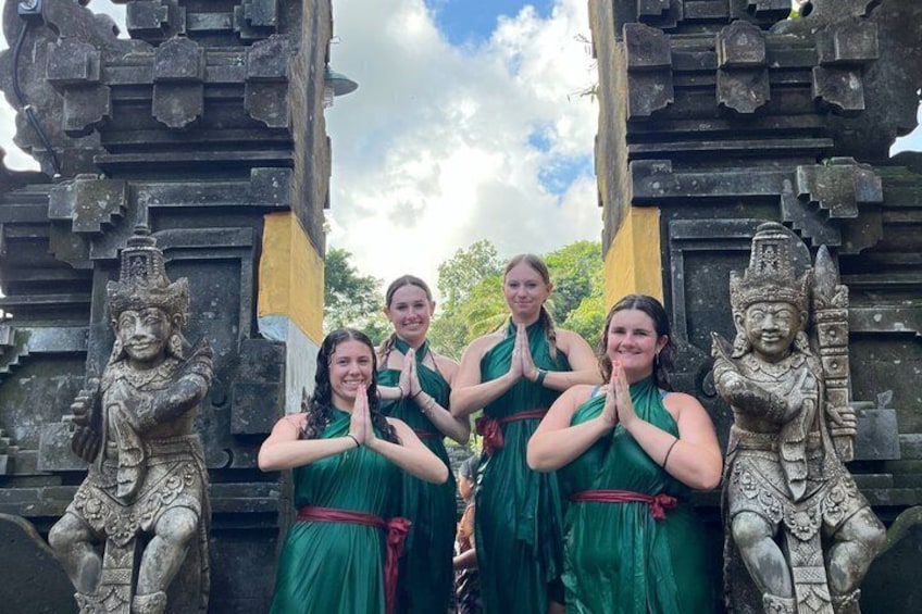 Entree van een tempel met vier mensen in groene jurken, een stenen beeld en een gele vlag. 2