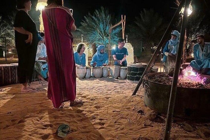 En gruppe mennesker spiller traditionelle trommer i et sandet udendørs miljø om natten. 4