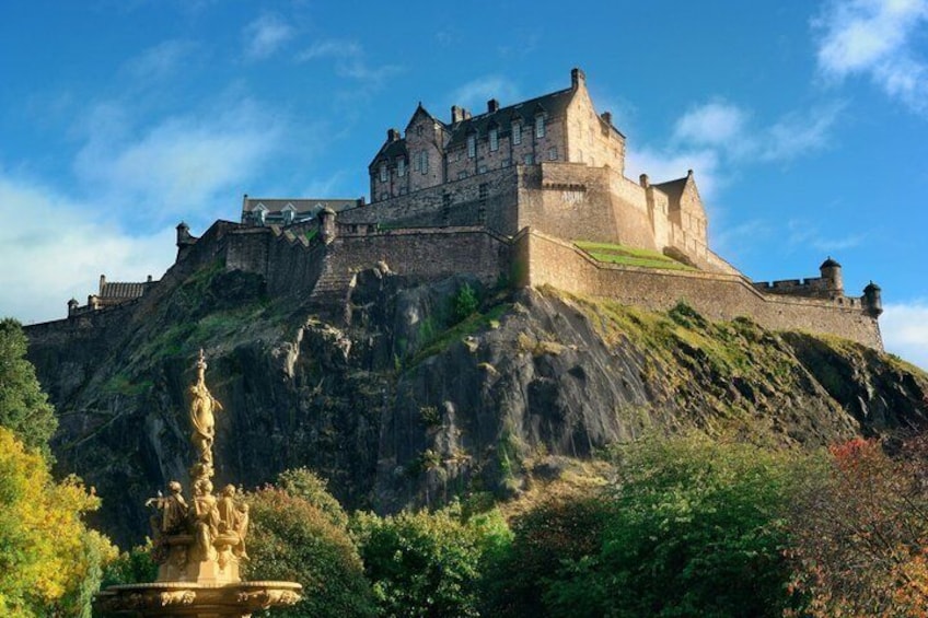 A historic castle on a hill with a statue in the foreground. 5