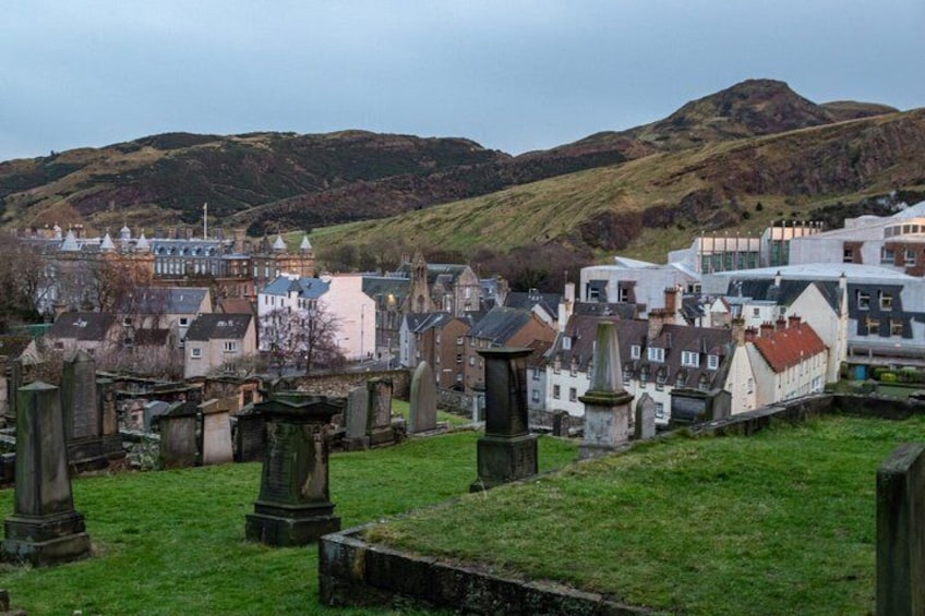 A cemetery with headstones and a town with buildings and hills in the background. 4