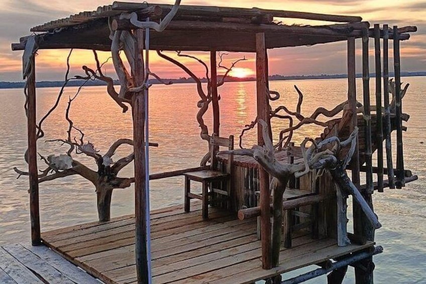 A wooden gazebo with intricate branches, overlooking a calm body of water during sunset. 3