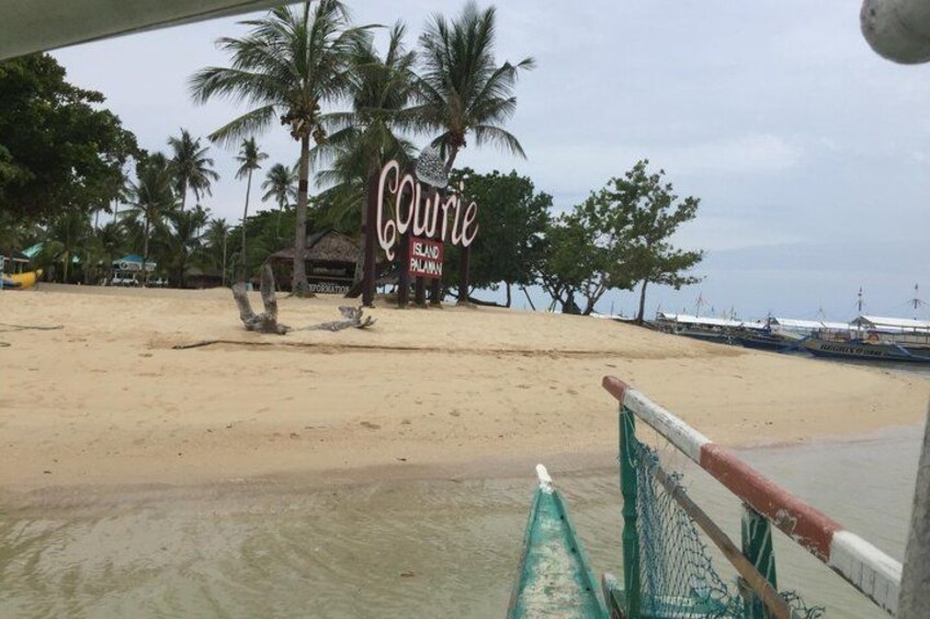 Una spiaggia con un cartello che indica 'Curry Island Palawan', palme e barche nell'acqua. 2
