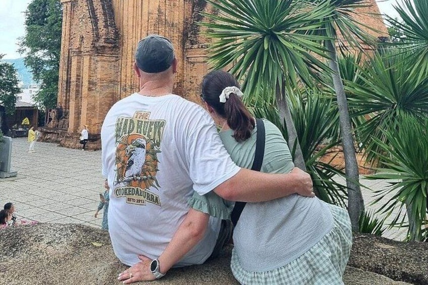 Dos personas abrazándose frente a un edificio histórico con palmeras. 1