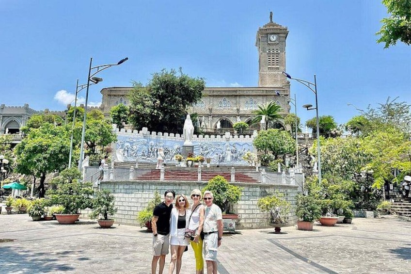 Un grupo de personas posa frente a un edificio histórico con una torre de reloj, rodeado de macetas con plantas y una fuente. 4
