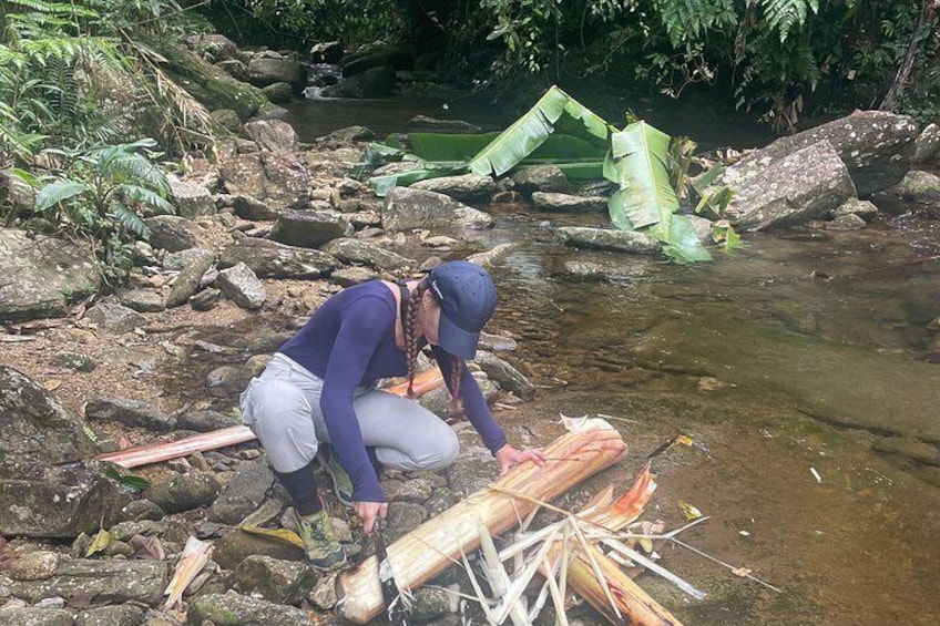 A person crouching by a stream, handling a large piece of wood and a bundle of straw. 2