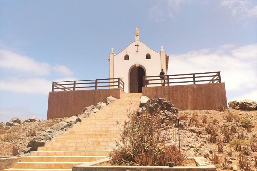 Eine Kirche mit Kruzifix, umgeben von einer Steinmauer und einem Holzzaun, mit einer Treppe, die zum Eingang führt. 3