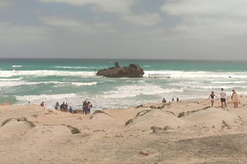 Ein Strand mit Menschen, die entlanggehen und stehen, Wellen, die auf das Ufer branden, und einem Felsen im Wasser. 5