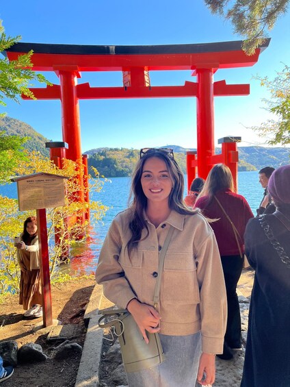 A person standing in front of a red torii gate with a lake and mountains in the background. 1