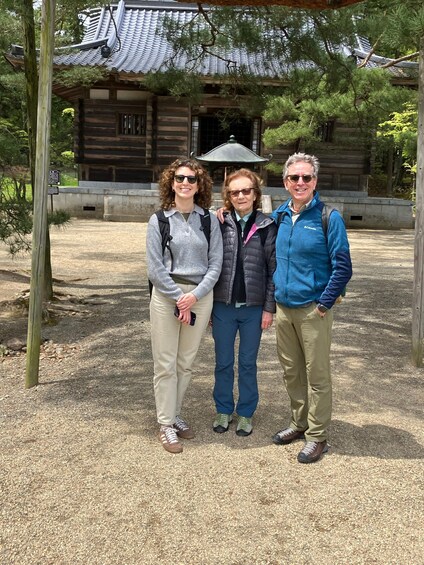 Three people standing in front of a traditional building with a tiled roof. 3