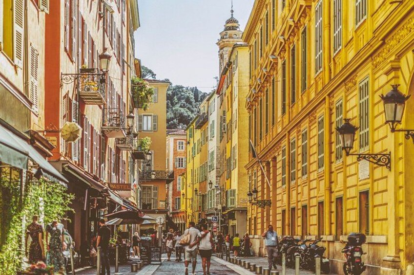 Una stretta via fiancheggiata da edifici colorati, con passanti e motociclette parcheggiate. 3