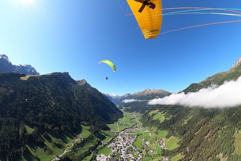 Een paraglider vliegt boven een vallei met bergen en een klein stadje eronder. 1