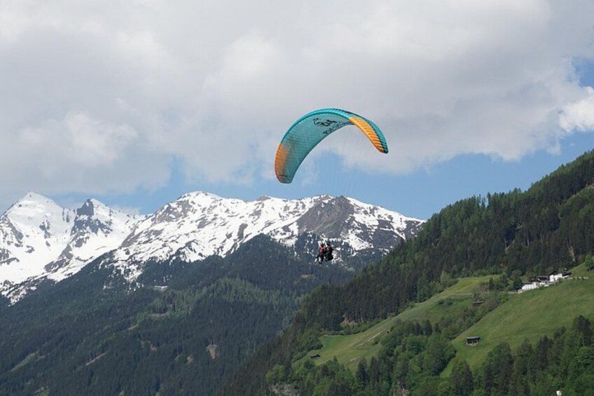 Een persoon paraglide boven een bergachtig landschap met besneeuwde toppen en dichte bossen. 2
