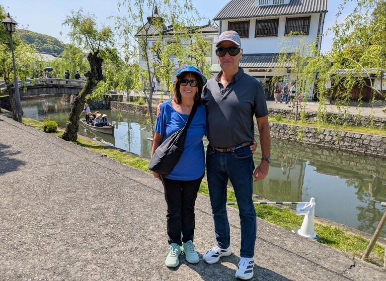 A couple standing by a canal with traditional buildings and a stone bridge in the background. 5