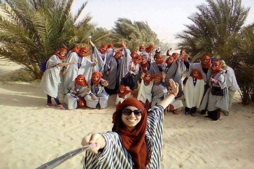 A group of people in traditional attire posing on a sandy beach with palm trees in the background. 3