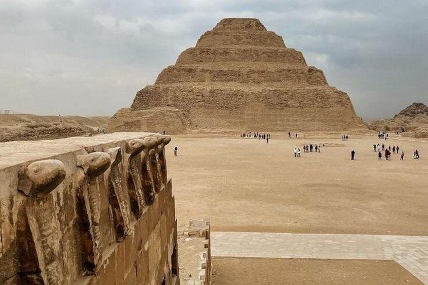 A large pyramid structure with a flat top, surrounded by a sandy area with people. 1