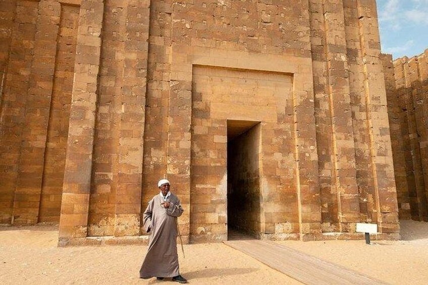 A person in traditional attire walking in front of a large, ancient stone structure with a doorway. 4