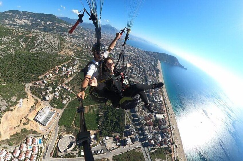 Eine Person gleitet mit einem Paragleiter über einer Küstenstadt, mit Blick auf das Meer und die Berge. 2