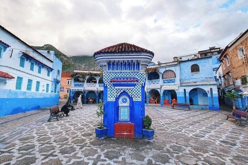 A blue building with a red door and a tiled roof in a cobblestone courtyard. 1