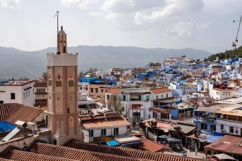 A town with a prominent tower, terracotta-roofed buildings, and a backdrop of mountains. 5