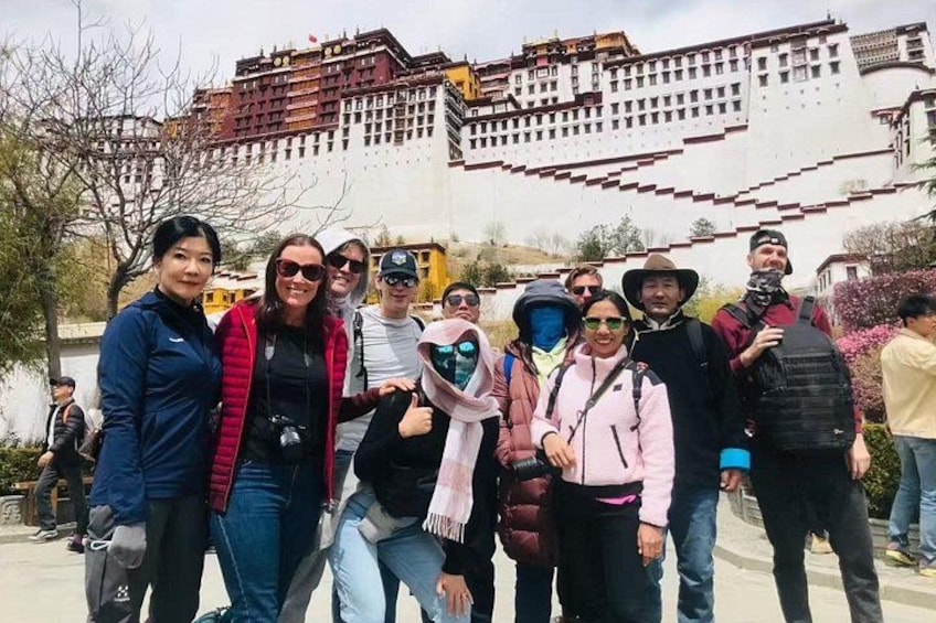 A group of people standing in front of a large, white, multi-tiered building with red accents. 1