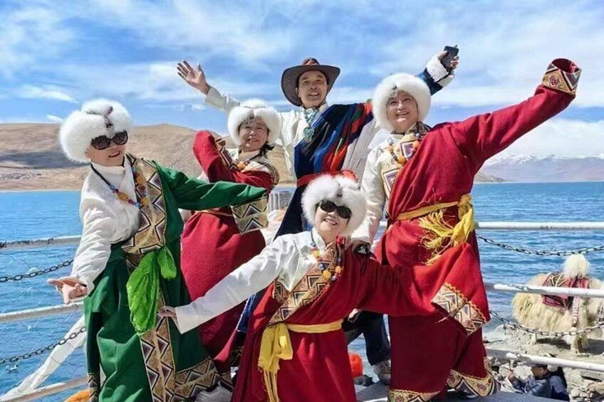 A group of people in traditional attire by a lake with mountains in the background. 4