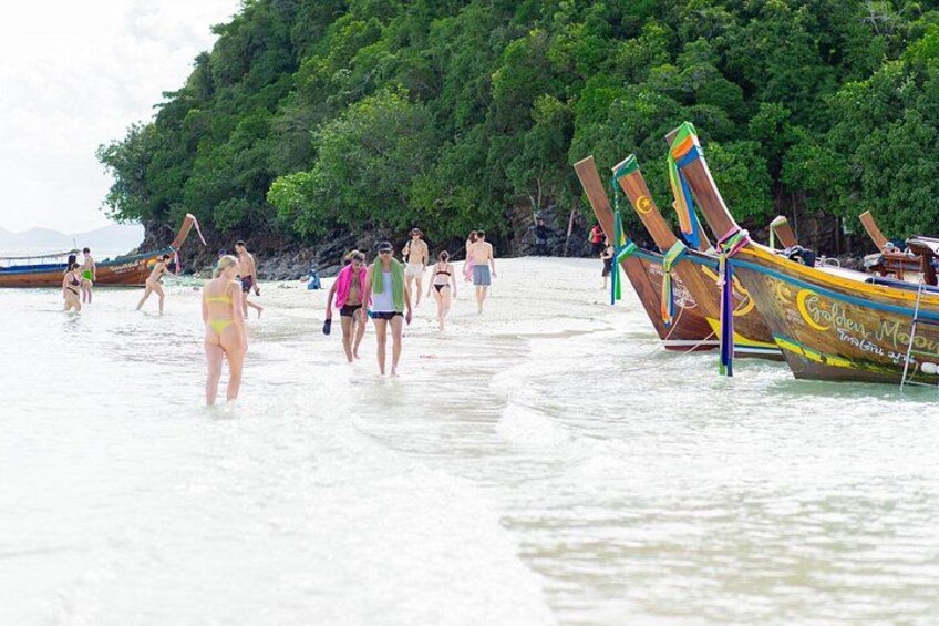 A beach with people walking and boats docked. 2