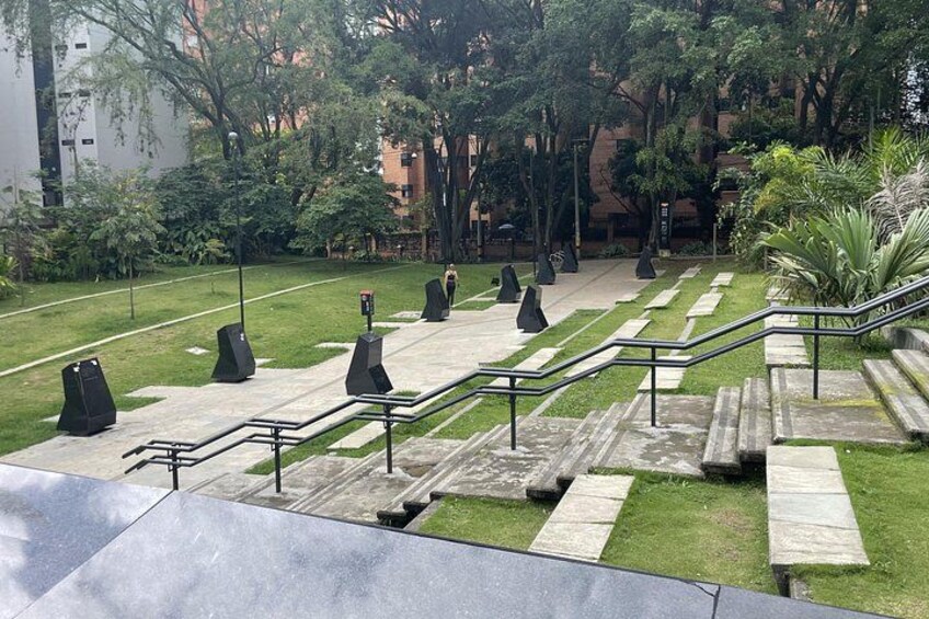 Un parque con una serie de escalones que conducen a una zona ajardinada, rodeada de árboles y edificios. 5