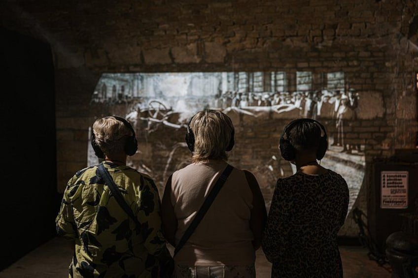 Tres personas observando una exhibición en una sala tenuemente iluminada con paredes de ladrillo. 5