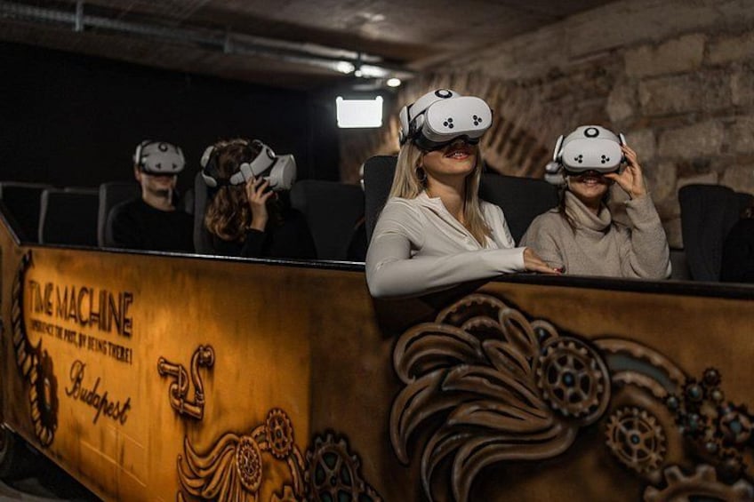 Personas con cascos de realidad virtual sentadas en una habitación con una mesa de madera que muestra un logo y texto. 4
