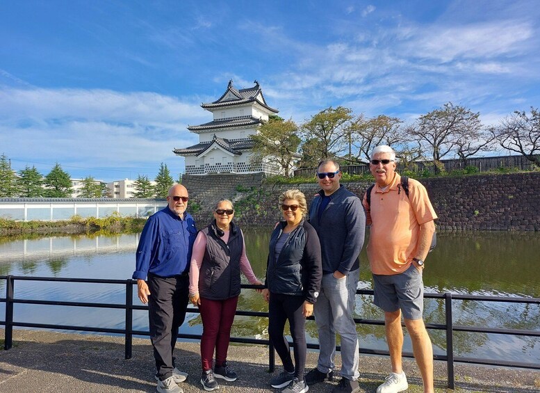 A group of people standing by a calm body of water with a traditional Japanese castle in the background. 5