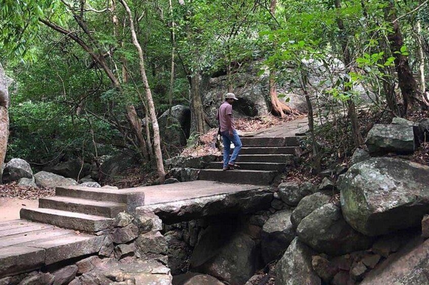 A person walking on stone steps in a forested area with large rocks and trees. 1