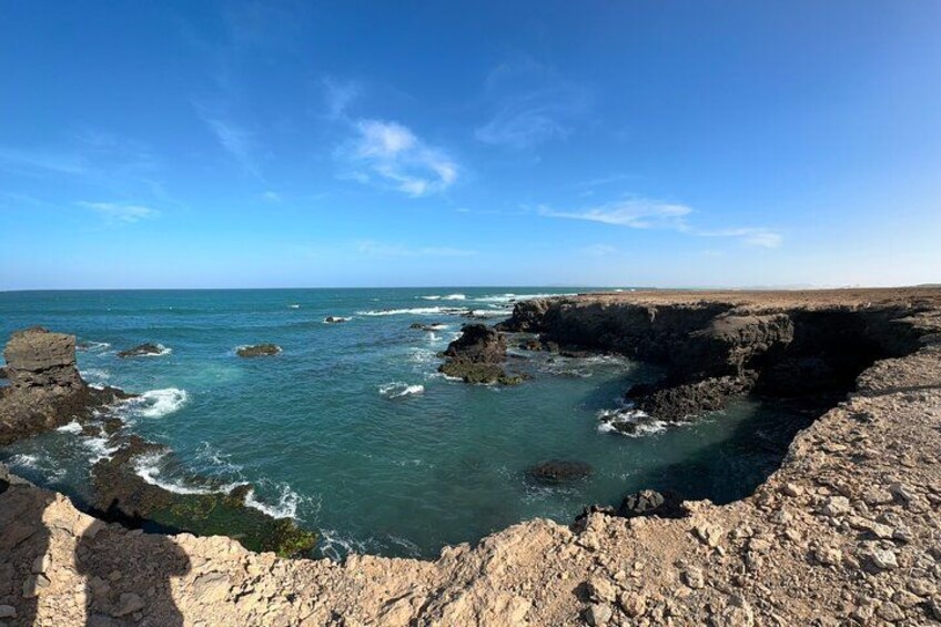 A rocky coastline with waves crashing against the rocks under a clear blue sky. 3