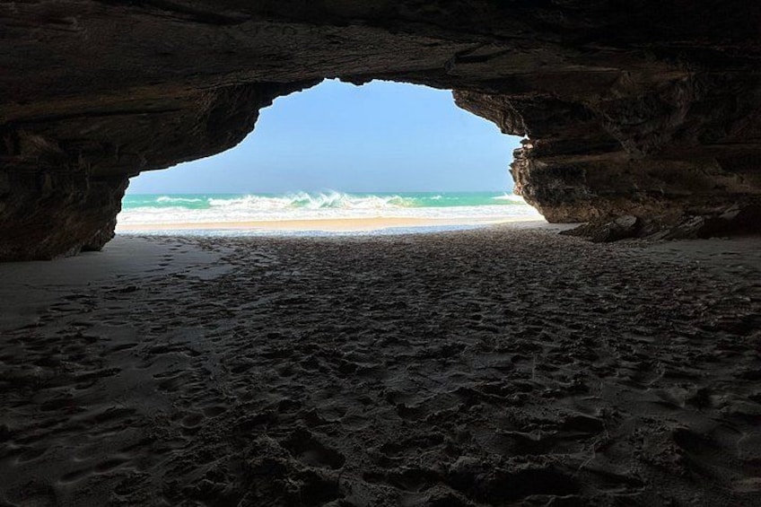 A beach with a cave entrance, sandy shore, and ocean waves. 4